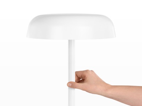 A hand touches the stem of a white Ode Lamp to turn it on or off.