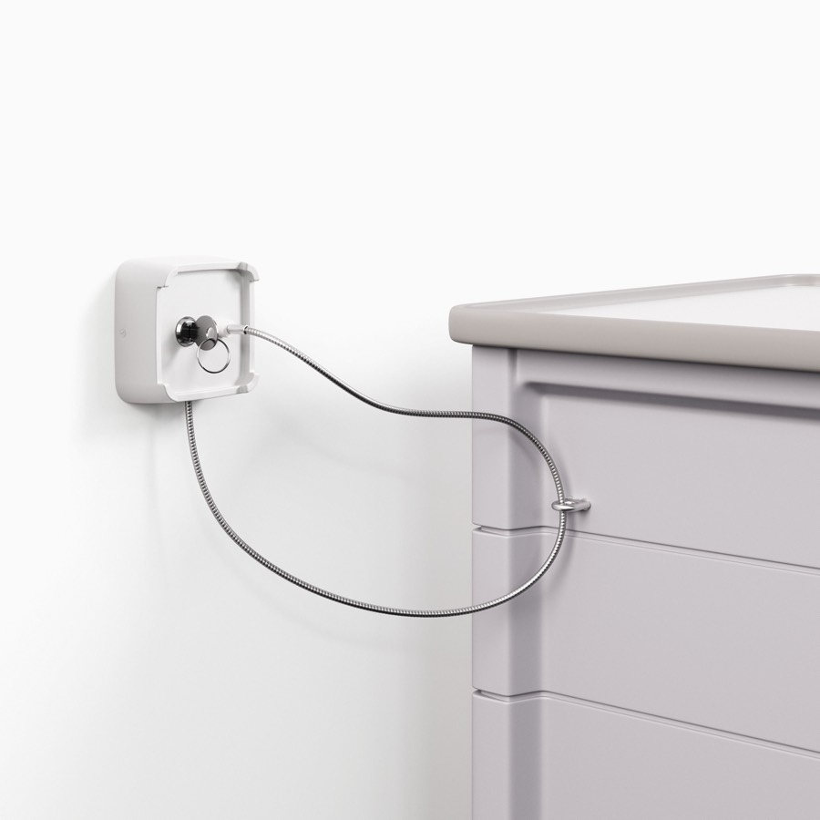 A lock attached to the wall with a metal wire running to and attached to a Procedure and Supply Cart in a light gray body.