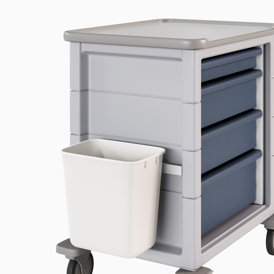 A supply cart in a light gray body and midnight blue drawers with an adapter rail attached to the side holding a trash receptacle.