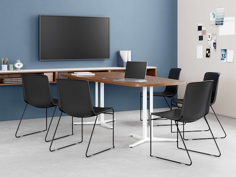 Black Pronta Stacking Chair in a conference room with an Everywhere Table, tv monitor, and storage cabinet.