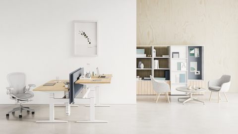 Een rug-aan-rug Ratio-bureau zowel op sta- als zithoogten met een lichtgrijze Aeron-stoel. Twee grijze Saiba-stoelen met een Civic-bijzettafel worden afgebeeld voor een Locale-boekenkast.