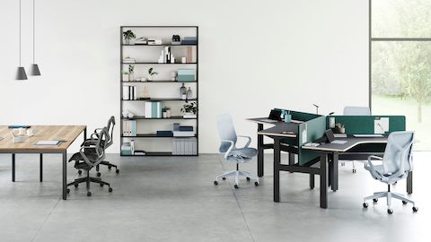 An open office environment with a cluster of three Ratio 120 desks positioned at varying heights to the right and a large Layout table on the left. A selection of high- and low-back Cosm chairs are positioned around the desks with a bookcase in the background.