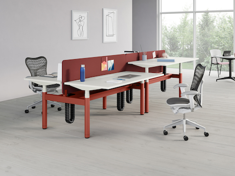 A cluster of four height-adjustable Ratio desks with white worksurfaces, privacy screens, and two gray Mirra 2 Chairs in an office environment. A Keyn Chair alongside a Civic Table are in the background.