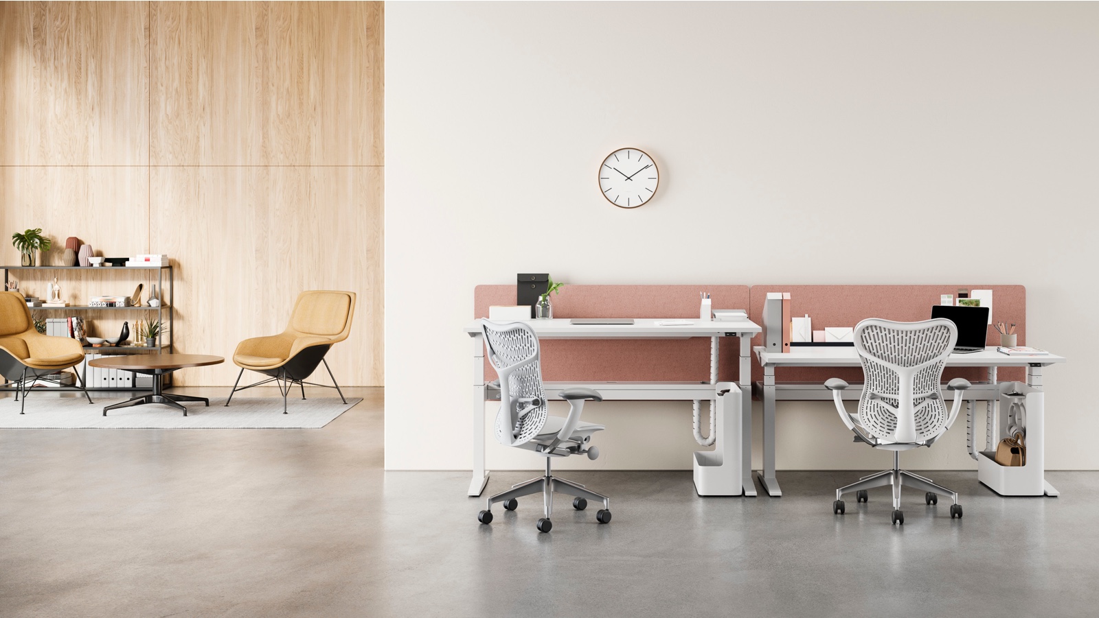 An office setting with a pair of Ratio desks in the foreground with white rectangular work surfaces and grey Mirra 2 chairs, and a lounge area with Striad lounge chairs, a Civic table and a bookcase in the background. One of the desks is raised to standing height.