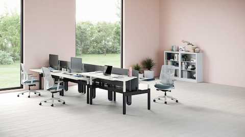 A bank of six Ratio desks with one positioned at a standing height. Three green and white Verus Chairs are set around the desks with a gray CK2 storage unit in the background. A bank of six Ratio desks with one positioned at a standing height. Three green and white Verus Chairs are set around the desks with a gray CK2 storage unit in the background.