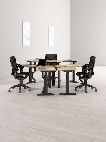 A cluster of three 120-degree Ratio height-adjustable desks, each with a black Cosm Chair.