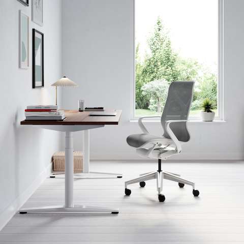A single Ratio desk with a dark wooden worksurface in a home office, featuring a light grey Cosm Chair. A wooden Paragraph Storage unit is in the background.