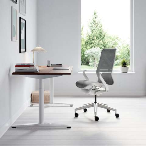 A single Ratio desk with a dark wooden worksurface in a home office, featuring a light gray Cosm Chair. A wooden Paragraph Storage unit is in the background.