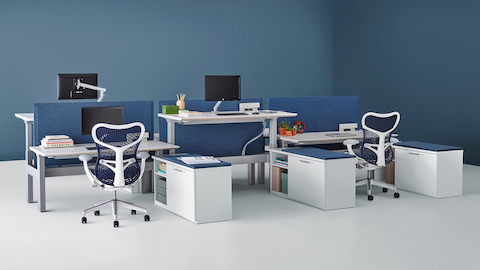 A Renew Link standing desk system with blue Mirra 2 office chairs, blue fabric divider panels, and lower personal storage. Two of the six desks are raised to standing height. A Renew Link standing desk system with blue Mirra 2 office chairs, blue fabric divider panels, and lower personal storage. Two of the six desks are raised to standing height.
