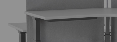 Primer plano de un sistema de escritorios elevados Renew Link con superficies de trabajo de 120 grados, patas en negro y acceso a energía de la superficie de trabajo.