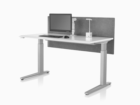 A single, white Ollin Monitor Arm holding a screen, attached to the work surface of a Renew Sit-to-Stand Table with a gray fabric privacy screen.