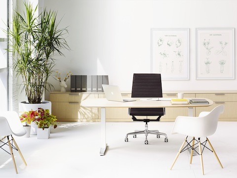 An office featuring an oval Renew Sit-to-Stand Table at a seated height, black Eames Aluminum Group Chair, and two Eames Molded Plastic Armchairs.