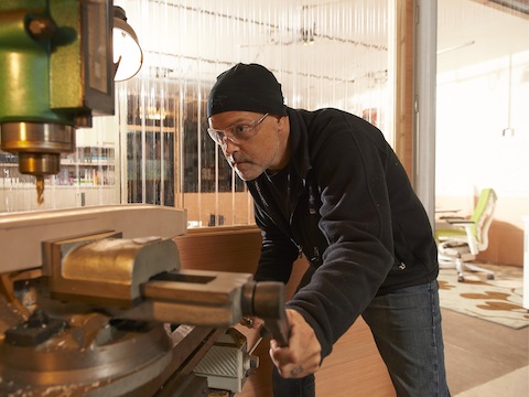 A photograph of Brian Alexander using a machine to cut a hole on a piece of wood.