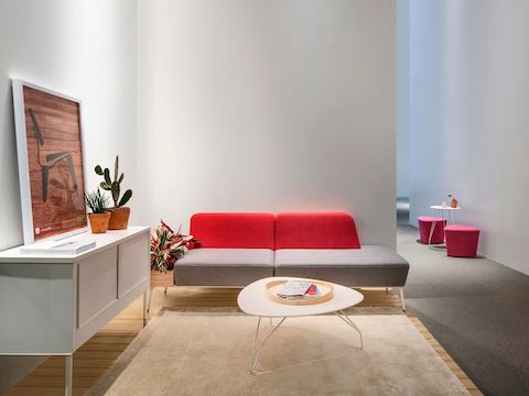 Um lounge em um espaço de trabalho com um sofá de dois lugares Sabha Collaborative vermelho e cinza e uma mesa de centro.