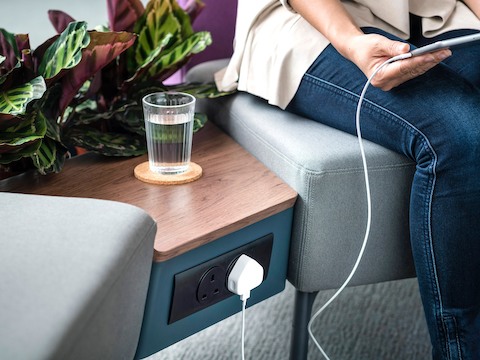 An office worker charges a device by plugging into a power outlet built into the surface between two Sabha seating modules.