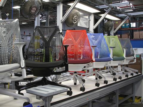 As costas suspensas de cadeiras Sayl cinza, preto, vermelho, azul e verde, prontas para serem inspecionadas na fábrica.