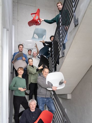Het Studio 7.5 ontwerpteam staat samen in een groep in een trappenhuis en houdt Zeph-stoelen vast.
