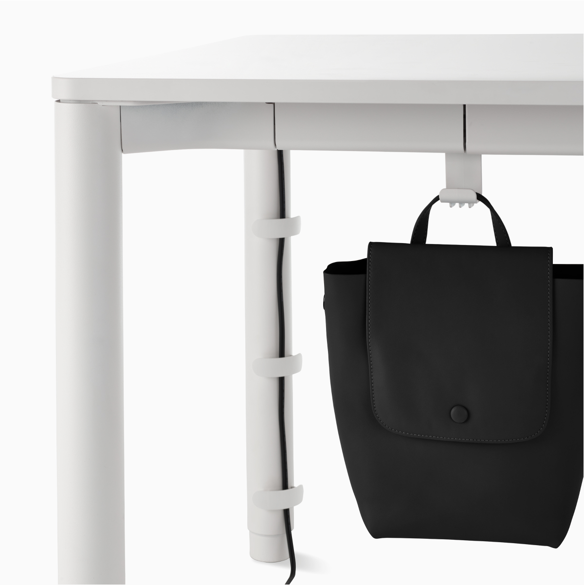 Detail of a black bag on a bag hook on a four leg height-adjustable table with a solid white surface and base.