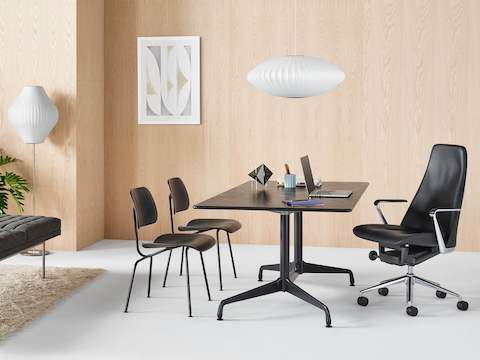 Um escritório executivo com uma cadeira Taper em couro preto, uma mesa retangular Eames e duas cadeiras Eames em compensado moldado.