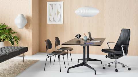 Una oficina ejecutiva con una silla Taper de cuero negro, mesa rectangular Eames y dos sillas de contrachapado moldeado Eames.