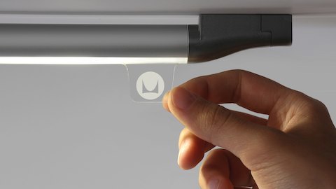Fingers grasp the tab of a Twist LED Task Light to control the illumination.