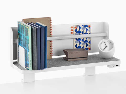 Une étagère Ubi attachée avec une toile de fond prend en charge les livres, un perforateur, une horloge de bureau et un module d'alimentation USB.