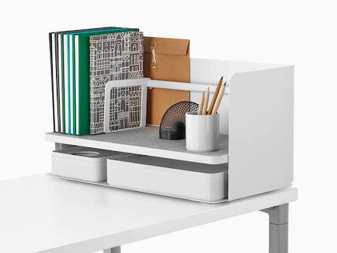 Een grote witte Ubi-desktoporganizer met een grijze antislipplank bevat boeken, een potloodbeker en twee opbergdozen.
