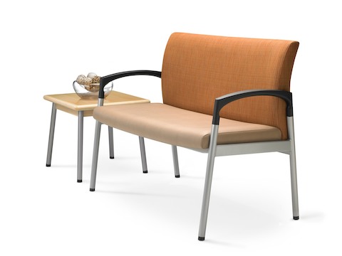 Angled view of extra-wide Valor Plus Seating with an orange back and beige seat, positioned next to a square end table.