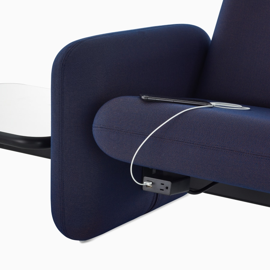 A close up view of a phone charging in a power module on a Wilkes Modular Sofa Group Sofa in dark blue.