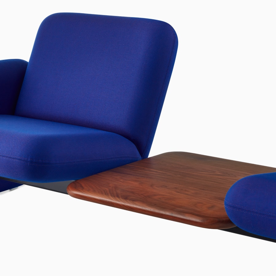 Visão aproximada em ângulo de uma mesa branca entre 2 assentos centrais de um sofá do Grupo de Sofás Modulares Wilkes em azul.