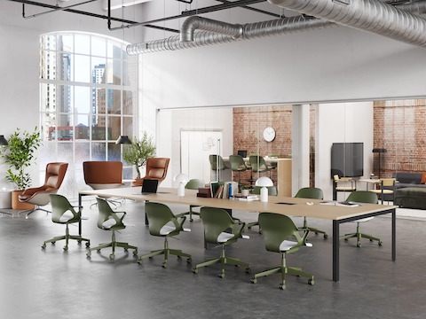 Doce sillas Zeph en oliva con almohadillas del asiento en gris claro alrededor de una mesa de proyectos en el medio de un espacio colaborativo con dos salas adyacentes.