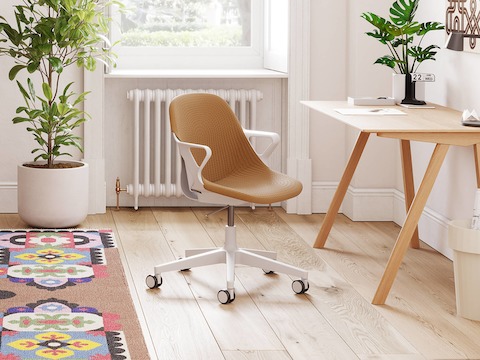 A light grey Zeph chair with a light brown knit cover is in front of a desk table in a small home office with plants.