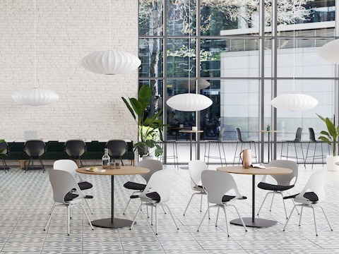 A Café that features light grey Zeph Side Chairs with a dark brown knit seat pad around round cafe tables, and a long modular sofa bordered with black Zeph Side Chairs with a green seat pad.