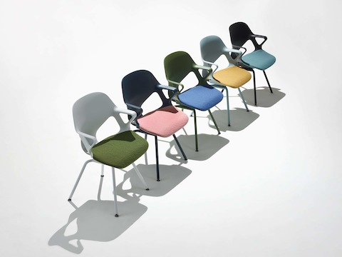 Vijf Zeph-bijzetstoelen met vaste armleuningen op een rij waaronder een alpine stoel met olijfkleurig zitkussen, een donkerblauwe stoel met roze zitkussen, een lichtblauwe stoel met geel zitkussen, een olijfkleurige stoel met blauw zitkussen en een zwarte stoel met lichtgroen zitkussen.