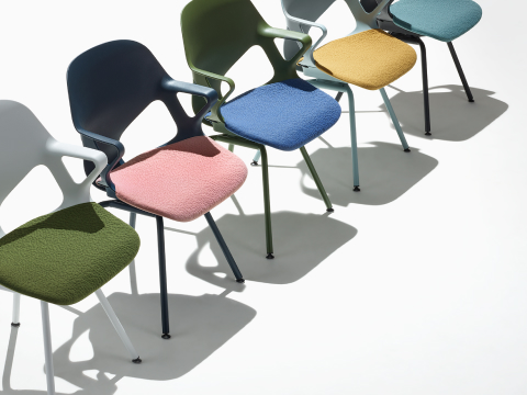 Cinco sillas para visitas Zeph con brazos fijos que forman una línea, la cual incluye una silla de color alpino con asiento acolchado de color verde oliva, una silla de color azul oscuro con asiento acolchado de color rosa, una silla de color azul claro con asiento acolchado de color amarillo, una silla de color oliva con asiento acolchado de color azul y una silla de color negro con asiento acolchado de color verde claro.