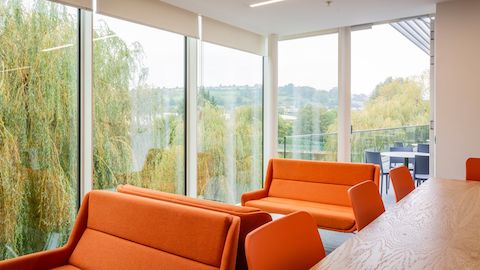 Hush-banken met oranje stofbekleding in een breakoutruimte en met zicht op stoelen op een balkon.