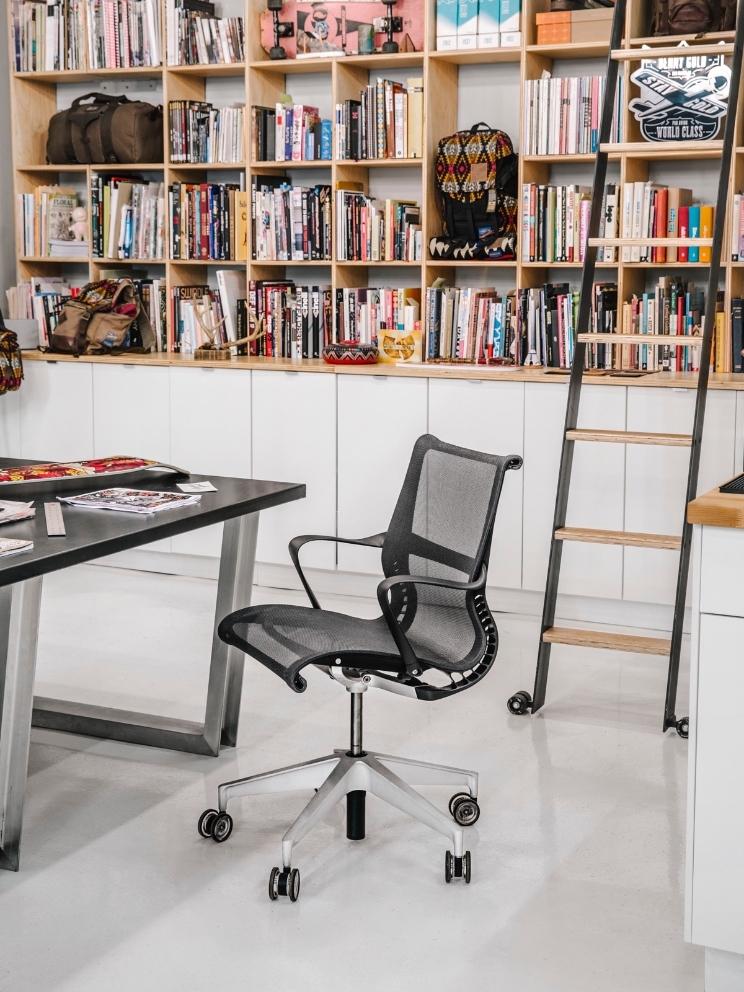 A Setu chair sits empty by a desk, with a large bookcase and ladder in the background. 