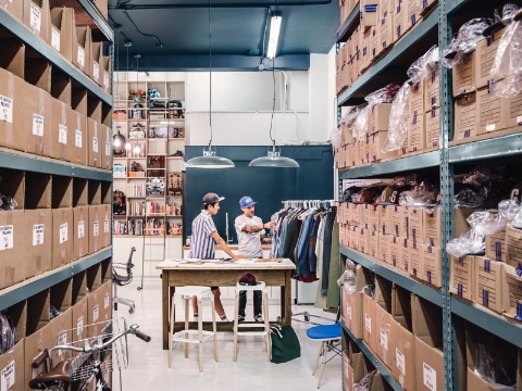 Two employees examine clothing products in an office warehouse area. 