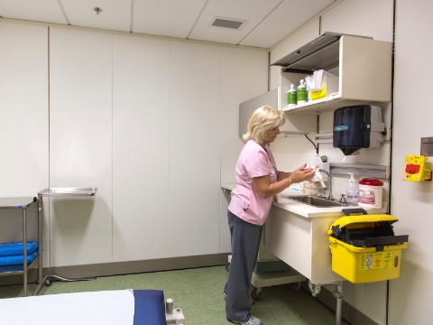 A woman washes her hands at a sink inside of an patient exam room. A woman washes her hands at a sink inside of an patient exam room.