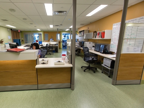 A woman works at her desk inside of a station within a medical facility. 