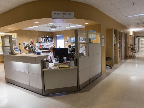 Two women converse at a corner care station inside of a medical facility. 