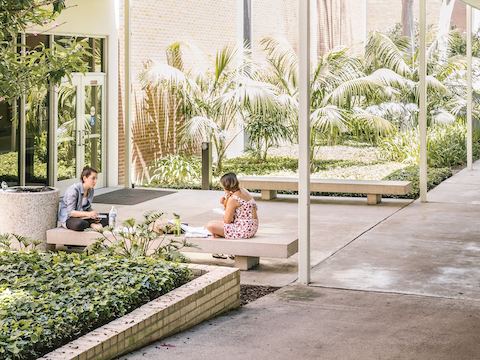 Two students talk while sitting on cement benches outside. Two students talk while sitting on cement benches outside.