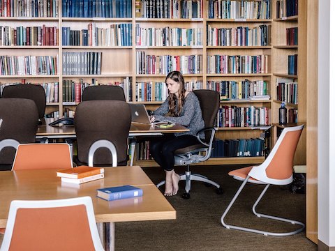 A student works on her laptop while sitting in a library.