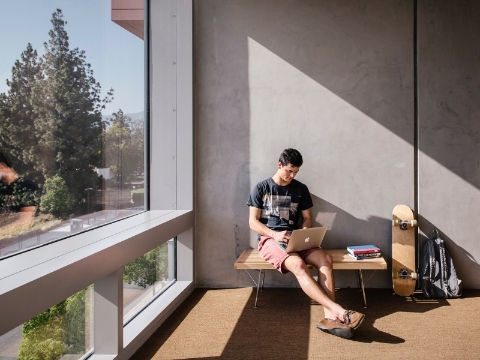 A student sits on a bench near a window while studying.