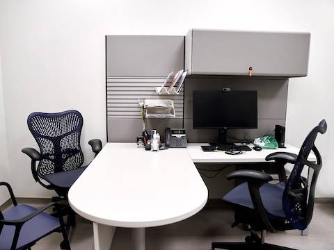 Sala de consulta con dos sillas Mirra 2 en azul y en gris, una vista de frente y la otra de costado, ubicadas en torno al sistema Ethospace en blanco y gris.