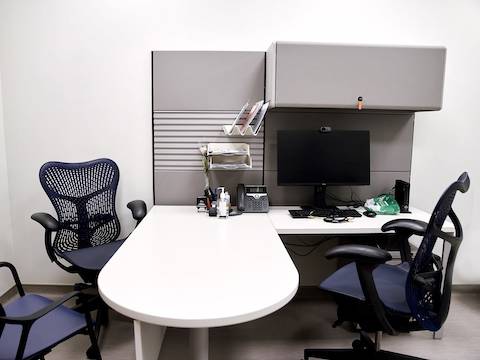 Consultation room with two Mirra 2 blue and grey chairs, one viewed from the front and second from a side positioned around Ethospace system in white and grey. Consultation room with two Mirra 2 blue and grey chairs, one viewed from the front and second from a side positioned around Ethospace system in white and grey.