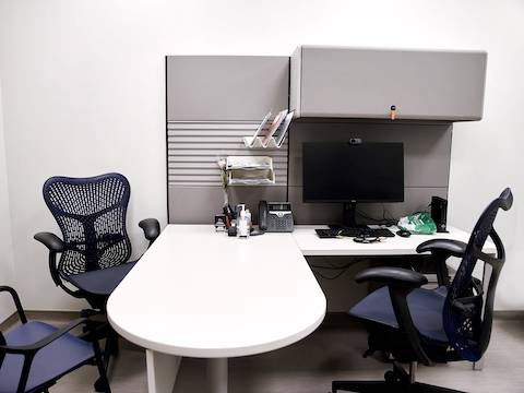 Consultation room with two Mirra 2 blue and grey chairs, one viewed from the front and second from a side positioned around Ethospace system in white and grey.