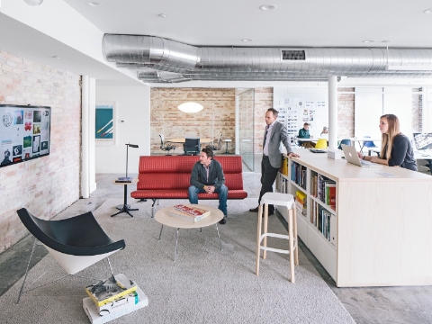 Employees gather in a cove space while viewing graphics on a video screen. Employees gather in a cove space while viewing graphics on a video screen.