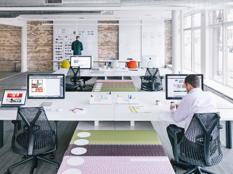 Empolyees among rows of tables and Sayl chairs inside of a shared workspace.