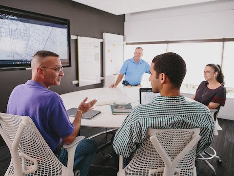 People sit in Sayl chairs at a conference table while talking. 